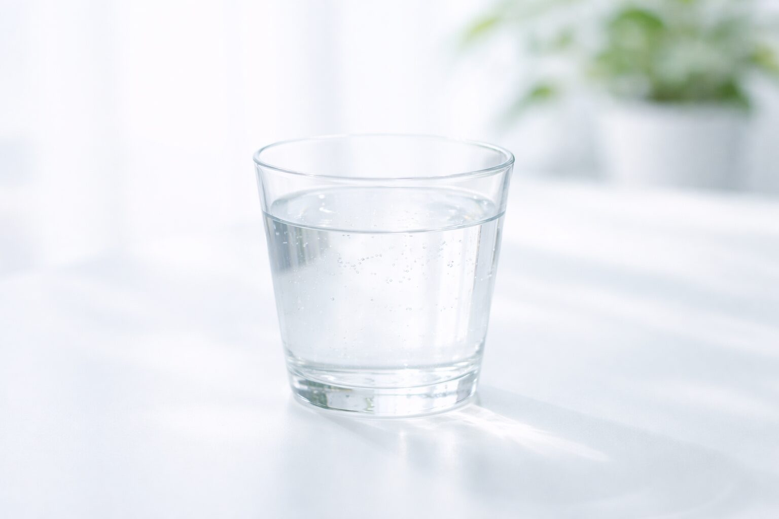 白い背景に置かれた透明なグラスの水。ドライマウス対策や唾液分泌改善をイメージした清潔感のあるビジュアル。